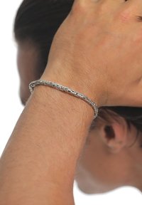 Silver metal bracelet with an intricate braided design, resting on a wrist; smooth texture and slender shape, reflecting light subtly.