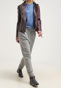 Brun läderjacka med hög krage, blå chambray skjorta, grå sweatpants och svarta ankelstövlar. Avslappnad passform med knappdetaljer.