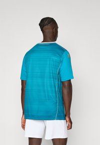 Ein kurzärmliges, türkisfarbenes Sporttrikot mit strukturiertem Design, weißen Akzenten und "Fiorentina"-Branding am hinteren Kragen.