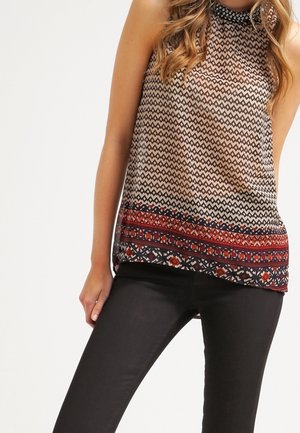 Bezrekawowy wzorzysty top z geometrycznymi wzorami w kolorach czarnym, beżowym i czerwonym, noszony z czarnymi dopasowanymi spodniami, pokazany od ramion do ud.