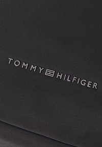 Tessuto nero con texture e marchio in rilievo "TOMMY HILFIGER", caratterizzato da un semplice logo rettangolare al centro, design minimalista.