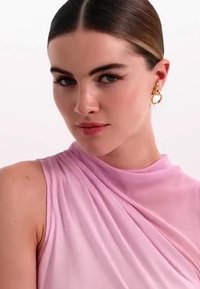 Haut rose sans manches avec un design drapé, fabriqué dans un tissu doux et lisse. Des boucles d'oreilles en or ajoutent une touche métallique.