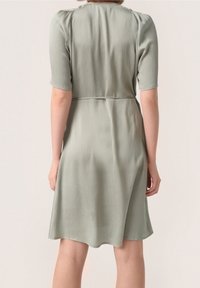 Světlounce zelené šaty s krátkými rukávy, strukturovaným materiálem, vyšitým pasem a sukní do áčkového střihu, která končí těsně nad kolenem.