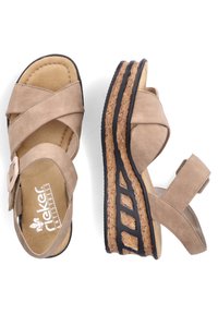 Sandali in suede beige con cinturini incrociati, fibbia regolabile e suola a zeppa in sughero stratificato e gomma nera. Soletta morbida e strutturata.