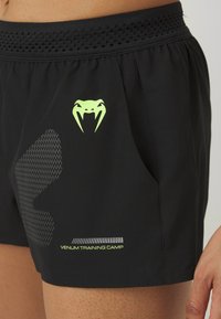 Crne atletske kratke hlače napravljene od laganog materijala s teksturiranim pojasom. Imaju zeleni zmijski logo i natpis "VENUM TRAINING CAMP".