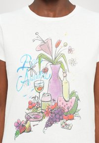 Illustration de nature morte sur un t-shirt blanc avec un vase rose de fleurs, un verre de vin, une canette de boisson, des raisins, une tranche de pastèque, des cerises et le texte "Bon Appetit".