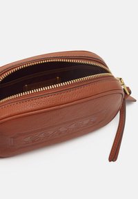 Pochette in pelle marrone con finitura texturizzata, dotata di chiusura con zip dorata, logo impresso e tracolla staccabile. Interno foderato.