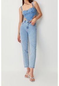 Top corto de mezclilla azul con escote corazón y cortes laterales, combinado con jeans de pierna recta de tiro alto. Azul claro, con un leve desgaste.