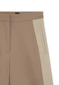 Broek met een mix van lichtbruin en beige stoffen, gestructureerd ontwerp en een zijzak op het beige paneel. Zachte textuur.