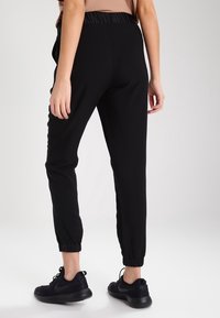Black jogger pants with a tapered leg, elastic waistband, and elastic cuffs. Paired with black sneakers, on a light gray background.