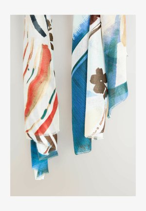 Multifarvede tørklæder i let stof med abstrakte mønstre i rød, blå og brun, med frynsete kanter, hængende mod en neutral baggrund.