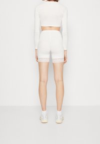 Haut court blanc et short assorti avec bordure en dentelle à l'ourlet. Le tissu est lisse, ajusté et extensible. Des chaussures de sport décontractées complètent la tenue.