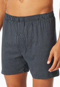 Marine-stripete boxershorts i lett stoff med elastisk linning og en enkelt knapp i front. Har tynne hvite vertikale striper.