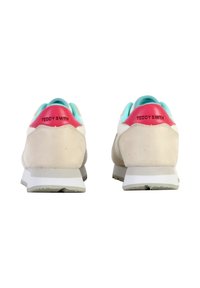 Une paire de baskets beiges avec des semelles blanches, une doublure intérieure turquoise et des languettes de talon rouges étiquetées "TEDDY SMITH", vues de l'arrière.