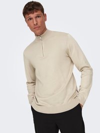 Beiger Sweater mit Reißverschluss am Kragen, mit gerippten Bündchen und Saum; weiche Stricktextur, schmaler Schnitt und ein Viertelreißverschluss am Kragen.