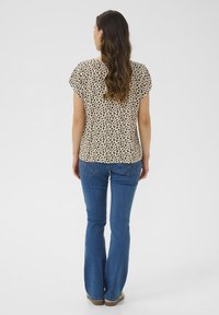 Haut à manches courtes en imprimé léopard beige et marron, associé à un jean évasé bleu à taille basse et accents métalliques.