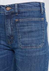 Mörkblå denimjeans har en klassisk passform, femfickorsdesign och orange sömmar längs sömmarna och midjebandet.