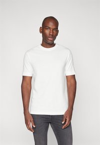 Weißes Baumwoll-T-Shirt mit kurzen Ärmeln und Rundhalsausschnitt, mit einer glatten Textur und einem taillierten Design, kombiniert mit grauen Jeans.