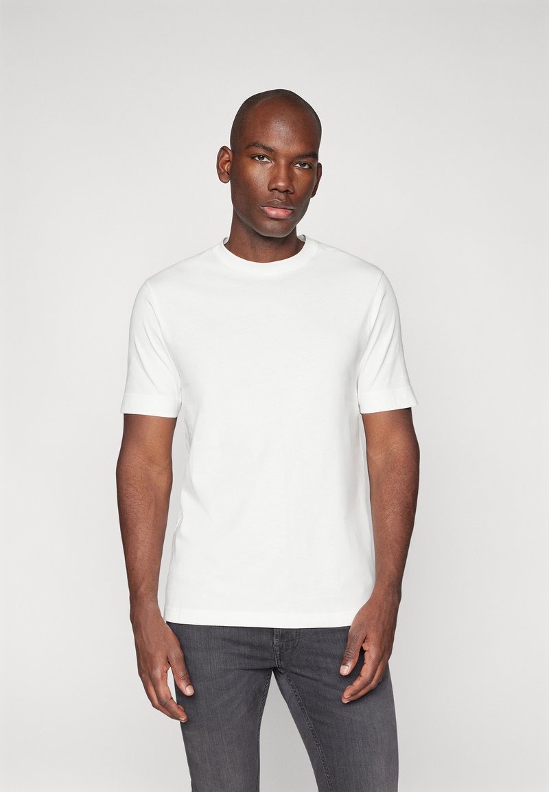 Weißes Baumwoll-T-Shirt mit kurzen Ärmeln und Rundhalsausschnitt, mit einer glatten Textur und einem taillierten Design, kombiniert mit grauen Jeans.