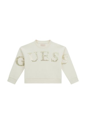 Sweat-shirt crème à manches longues avec le mot "GUESS" écrit en grandes lettres dorées à sequins sur le devant et les manches.