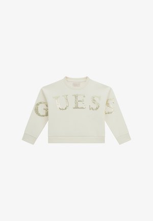 Sweat-shirt crème à manches longues avec le mot "GUESS" écrit en grandes lettres dorées à sequins sur le devant et les manches.