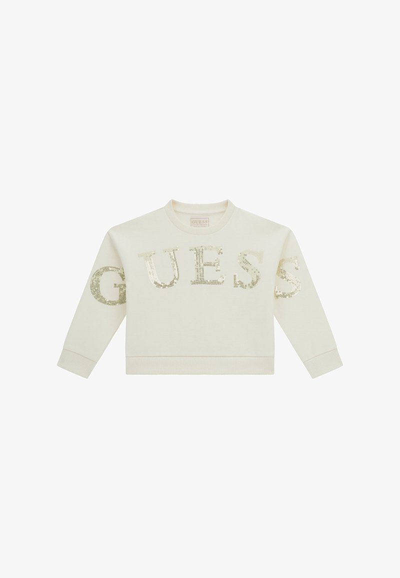 Sweat-shirt crème à manches longues avec le mot "GUESS" écrit en grandes lettres dorées à sequins sur le devant et les manches.