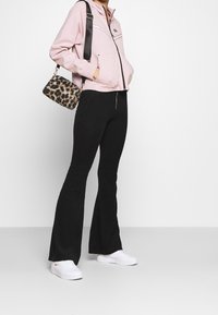 Giacca con cappuccio zip up rosa chiaro con righe bianche, pantaloni flared neri a coste, sneakers bianche e borsa leopardata.