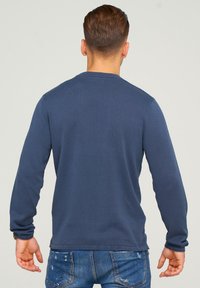 Camisa de manga larga azul marino con cuello redondo, hecha de un material suave y con un corte regular, combinada con jeans de mezclilla.
