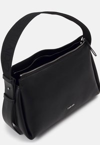 Černá kožená taška se zipovým uzávěrem, širokým popruhem s názvem značky a elegantním obdélníkovým designem. Přítomný minimalistický detail loga.