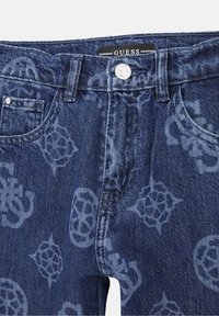 Jeans dżinsowe marki Guess w ciemnoniebieskim kolorze z subtelnym wytłoczonym wzorem logo. Posiadają przednie kieszenie i zapięcie na srebrny guzik.