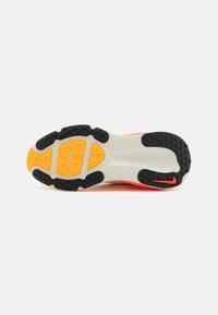 Suela de zapato con un diseño de caucho negro, amortiguación naranja y base gris con patrones texturizados para tracción. Acentos brillantes en el diseño.