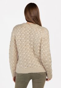 Beiger Strickpullover mit strukturiertem Muster, ausgestattet mit einem gerippten Saum und Bündchen. Die Rückansicht zeigt eine lockere Passform und einen Rundhalsausschnitt.