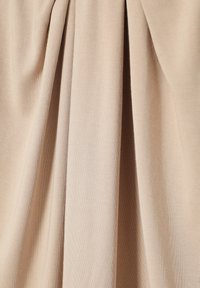 Tessuto beige con morbide pieghe verticali e texture liscia, che mostra materiale drappeggiato alla luce naturale.