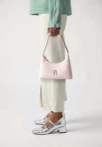 Sac à main en cuir rose avec un design incurvé, arborant une lettre "A" dorée et une fermeture éclair. Chaussures métalliques argentées avec un talon bloc.