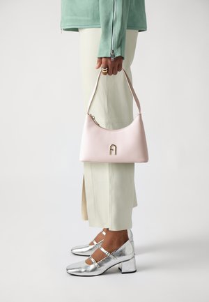 Rosa Lederhandtasche mit geschwungenem Design, ausgestattet mit einem goldenen Buchstaben "A" und einem Reißverschluss. Silbernmetallische Schuhe mit Blockabsatz.