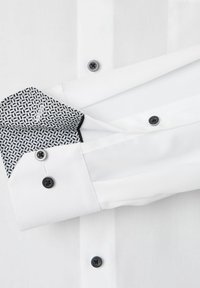 Biała koszula z wzorzystymi czarnobiałymi mankietami. Posiada czarne guziki i gładką teksturę materiału. Starannie skrojony, elegancki design.