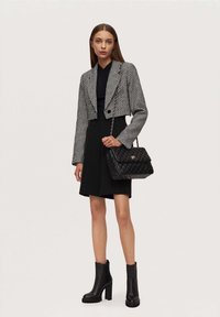 Black and white houndstooth cropped blazer, black top and flared skirt, quilted black handbag, and black heeled ankle boots.