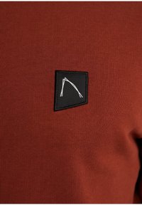 Tissu rouge côtelé avec un patch noir orné d'un motif géométrique blanc. Vue en gros plan mettant en valeur la texture et le contraste des couleurs.