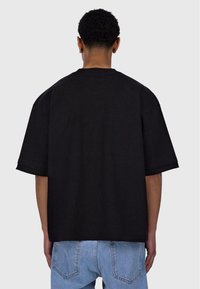 Schwarzes, oversized T-Shirt mit kurzen Ärmeln, aus Baumwolle. Mit Rundhalsausschnitt und glatter Textur. Zweifarbiger Stil mit minimalen Details.