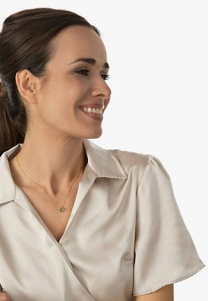 Hellebeige Satinbluse mit Kragen und puffierten kurzen Ärmeln. Sie hat eine zarte goldene Halskette mit einem kleinen Anhänger.