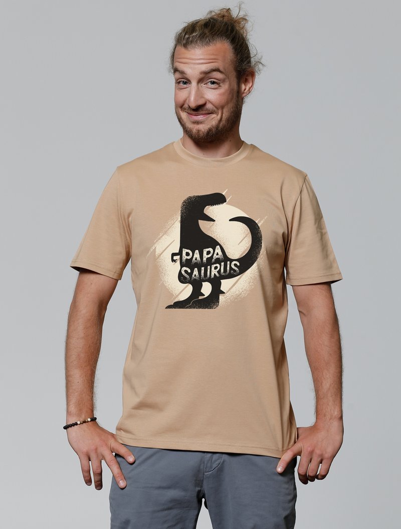 Beige katoenen T-shirt met een zwarte dinosaurusschildering en de tekst "PAPA SAURUS" in een speelse lettertype, met een zachte textuur.