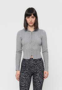 Gray cropped zip-up cardigan with cable-knit design, hood, and ribbed cuffs, paired with black and gray zebra-striped leggings.