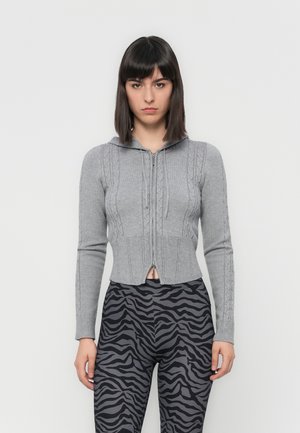 Gray cropped zip-up cardigan with cable-knit design, hood, and ribbed cuffs, paired with black and gray zebra-striped leggings.