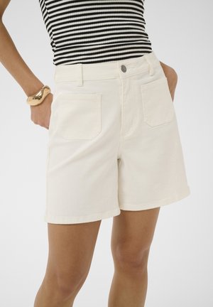 Kvinde iført off-white højtaljede cowboyshorts med forlommer, kombineret med en sort- og hvidstribet ærmeløs top og guldbøjle.