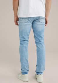 Gai zila džinsa bikses ar sašaurinātu piegriezumu, kurām ir aizmugurējie kabatas un viegla izbalēšana. Valkātas ar baltām sporta kedām un vienkāršu baltu T-kreklu.