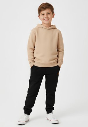 Beżowa bluza z kapturem z kieszenią typu kangur, czarne spodnie dresowe z prążkowanymi ściągaczami i białe sneakersy z czerwonymi akcentami. Prosty, casualowy design.