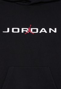 Schwarzer Kapuzenpullover mit großem weißen "JORDAN"-Schriftzug und rotem Jumpman-Logo. Mit einer Fronttasche und einem weichen, strukturierten Stoff.
