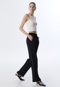 Czarne szerokie spodnie z elastycznym paskiem i sznurkiem, zestawione z dopasowanym białym topem crop. Gładki materiał o prostym wzorze.