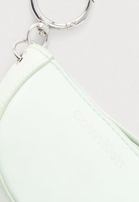 Παστέλ πράσινο δερμάτινο πορτοφόλι για κλειδιά Calvin Klein με ασημένιο κρίκο και κλείδωμα, τοποθετημένο σε λευκό φόντο.
