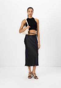 Top corto negro acanalado combinado con una elegante falda midi de satén negra y tacones negros con tiras. Sosteniendo un pequeño bolso de mano beige.